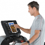 A fit man in athletic attire walking on the Landice L8 Treadmill setting up his workout on the screen