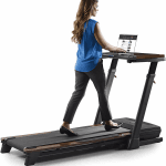 A woman in business casual attire walking on the Nordictrack Treadmill desk while working on a laptop